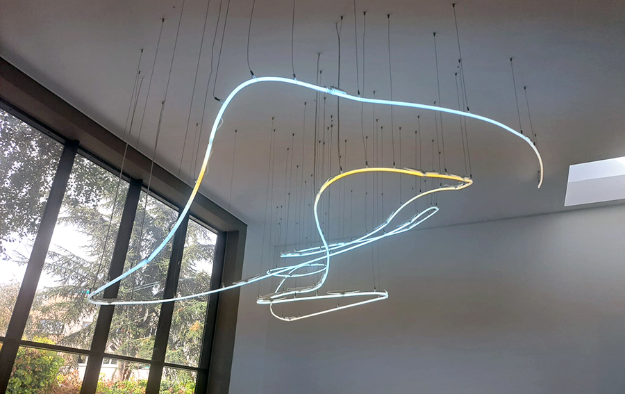 Lustre lumineux en trait néon suspendu sur les filins d'acier.
