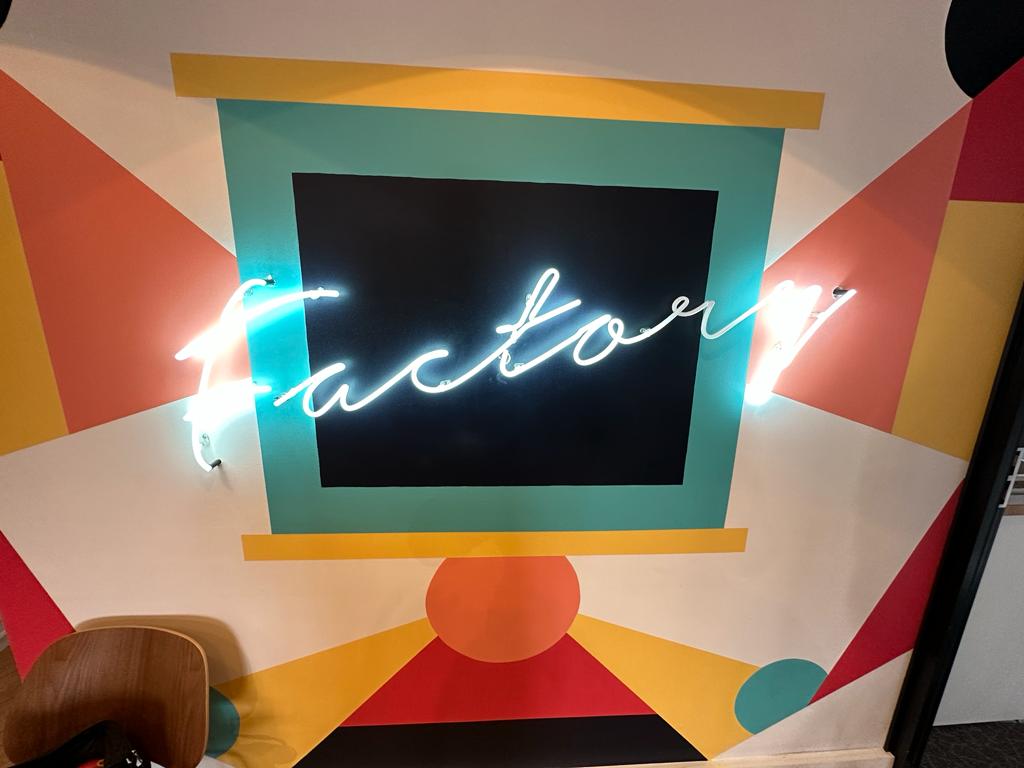 Logo mural "Factory" en écriture néon fine.
